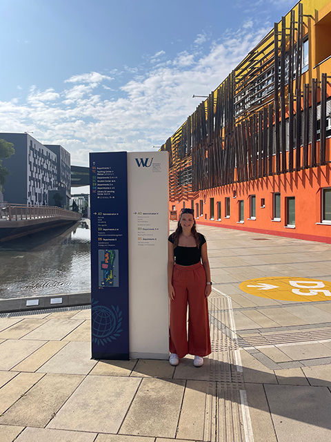 A girl stands next to a wayfinding sign in front of a colorful, modern looking building.