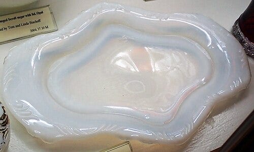 A Dresser Tray (circa 1899–1901) “1280 Winged Scroll” Opal. Commonly called milk glass. An opaque white glass. Heisey’s exhibits a large amount of “fire” when held to the light. Presented by James St. John Wikimedia Commons Image License