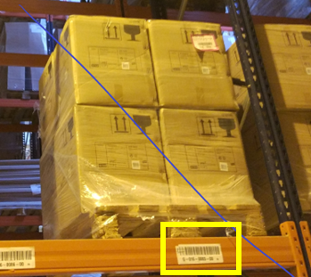 A photograph of a pallet location in a warehouse, focusing on a yellow highlighted barcode label on the shelf. The label includes a code and identification details. Above the shelf are stacked boxes, and a blue line visually highlights the label’s position, aiding in the identification of storage locations.