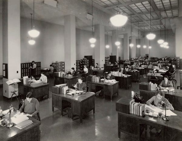 Black and White photograph from 1937 of the US Division of Classification and Cataloging. Long rows of desks with staff processing paperwork at each desk.