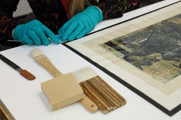 A conservator wears gloves while trying to repair a corner of one of the prints from ???The Mask and the Cross??? exhibition.