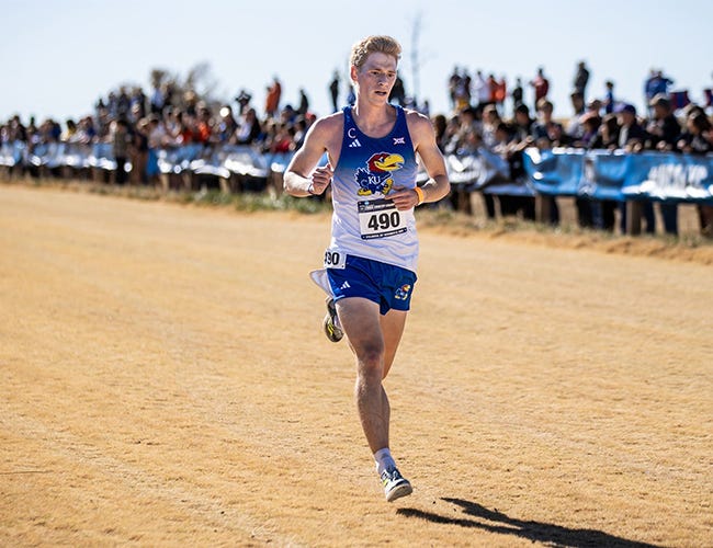 A man wearing a University of Kansas track uniform runs during a cross country event.