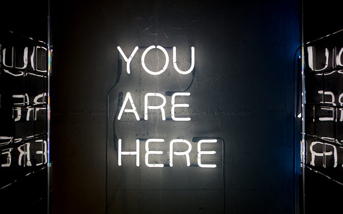sign showing you are here words in neon lights. Now is time.