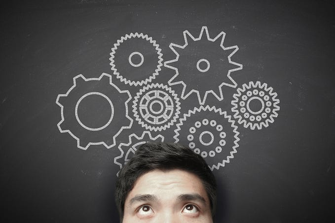 A man underneath a chalkboard with gears drawn on it.
