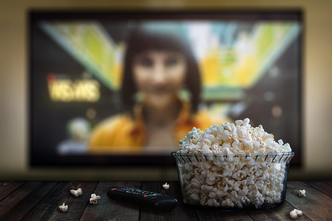 A TV showing a Netflix show in the background and a remote control with pop corn in the foreground