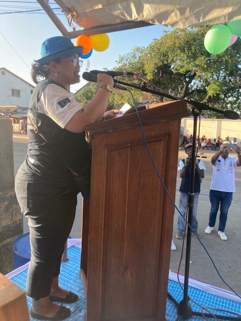 A black woman is standing up on a stage speaking in a microphone at a lectern. This woman is Dr Annick Andriamaro.