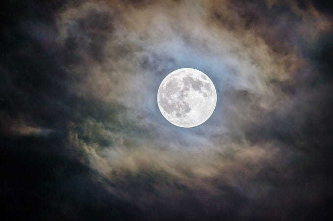 Bright, full moon peeping through a cloudy night sky.