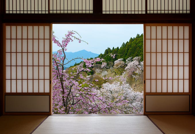 View of weeping cherry trees and hills through open paper doors of Japanese house.
