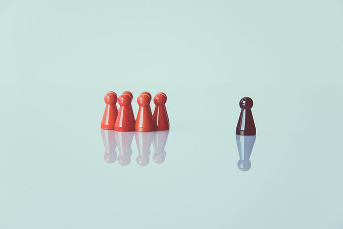 A group of 8 red game pieces huddles together while a single brown game piece stands some distance away from the group.