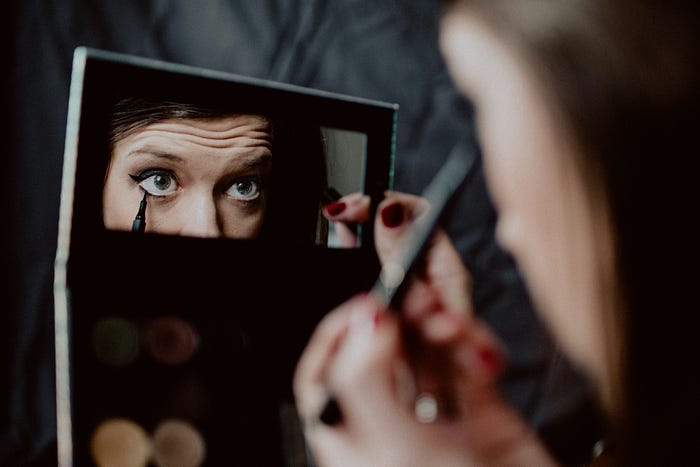 A female doing her makeup in a compact mirror.