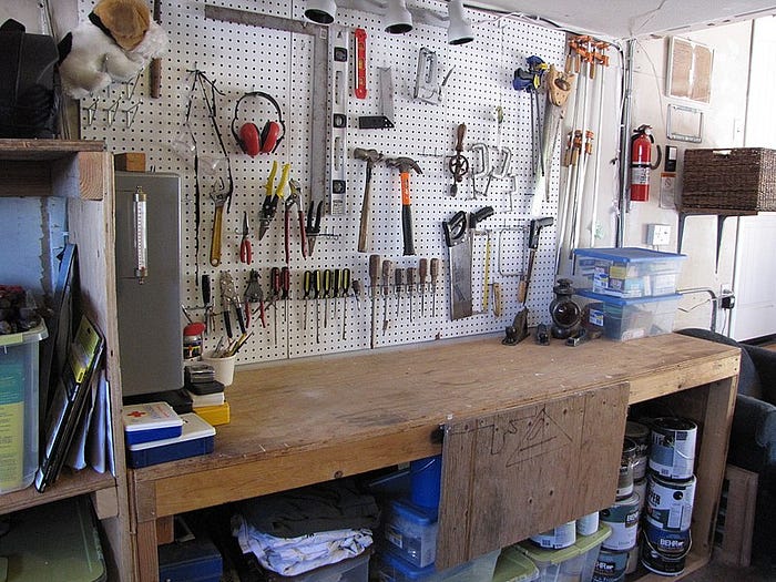 A workbench with a pegboard behind it. from the pegboard hang an array of hand-tools.