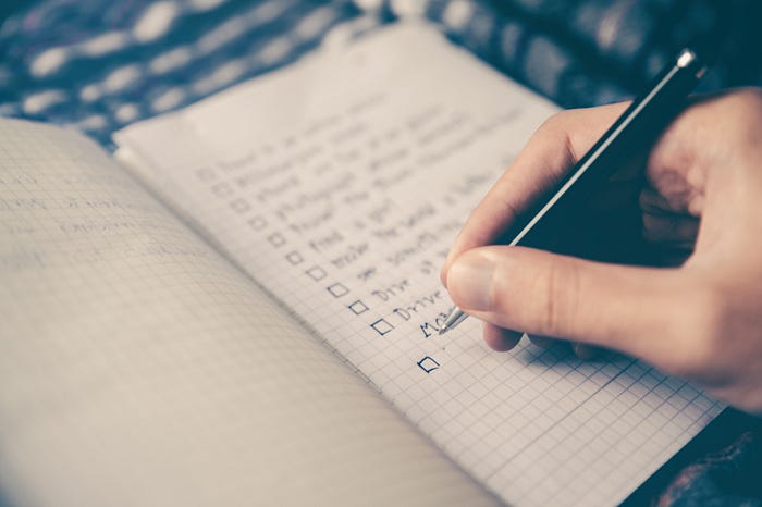A hand holding a pen makes a checklist in a notebook with a gridded page