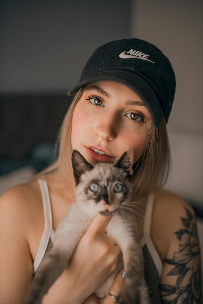 A woman, wearing a baseball cap, holding a cat, looking happy