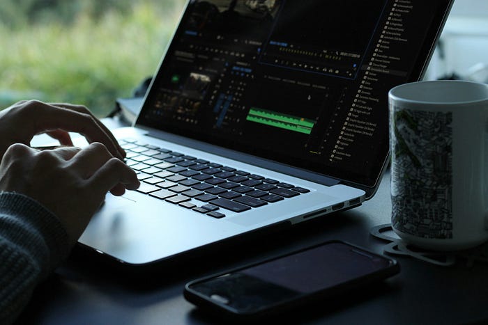 A close-up shot of a man’s hand video editing with a mug beside the laptop.