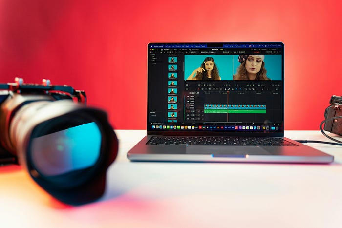 Video editing on a laptop and a camera lens on the side.