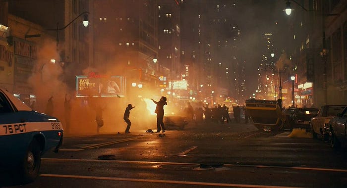 Kerusuhan di tengah jalan, ada mobil terbalik, orang-orang berdansa di tengah mobil yang terbakar