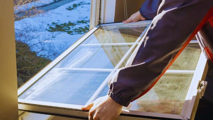 Worker installing a double-pane window unit in a Bluffton, SC, home on a cool day, carefully setting the window into the rough opening to illustrate professional window replacement services.