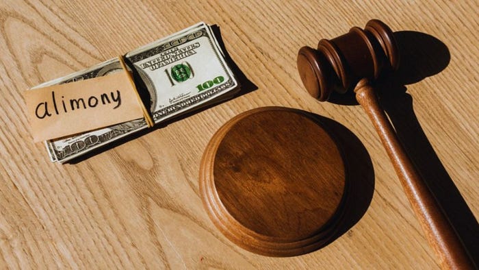 A gavel and money on a wooden table, with the word "alimony" prominently displayed.