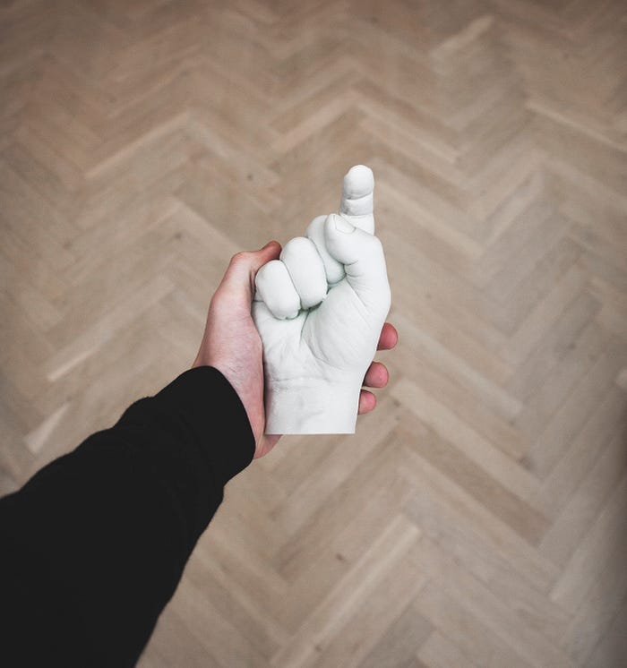 Hand holding a ceramic hand in a fist shape with index finger pointing