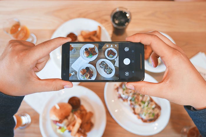 two hands holding a phone camera taking a picture of food