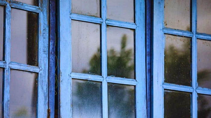Close-up of multi-pane, weathered blue window frames with cloudy glass, indicating sticking hardware and difficulty opening or closing.