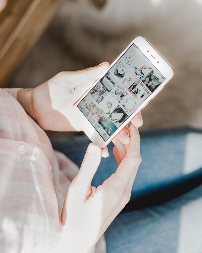 A woman holding her phone with her two hands. She is browsing social media