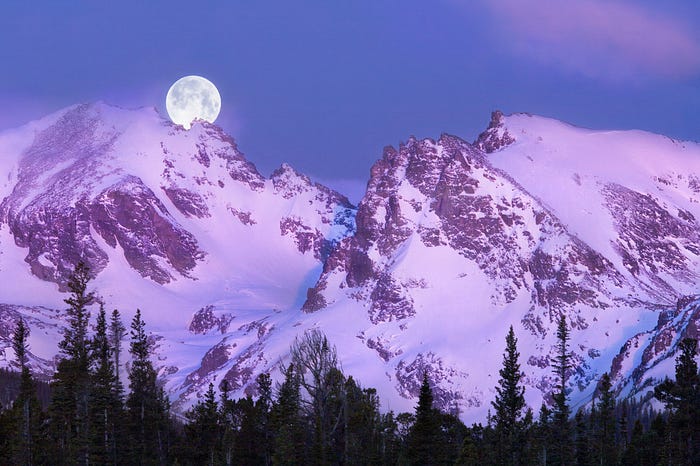 The setting moon on a snowcovered purple mountain.