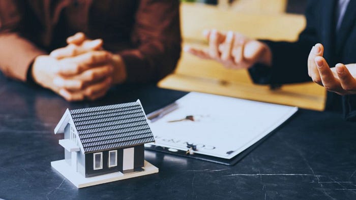 A Hilton Head realtor and client sitting at a desk discussing a property contract, with a model house and paperwork in focus, representing a real estate consultation.