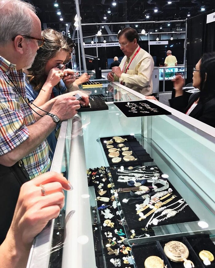 Visitors examining jewelry pieces at a global jewelry exhibition display counter during a trade show – The Jewelry Gossips