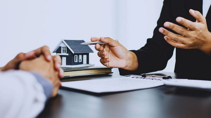 A real estate agent and a client hold a house model, illustrating their discussion about potential home purchases.