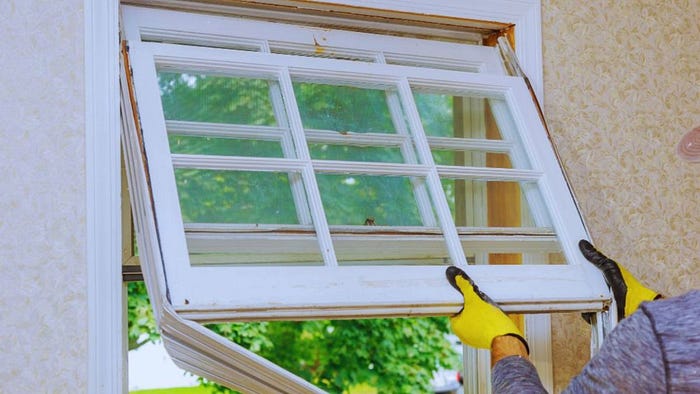 Worker removing an old residential window frame during a Bluffton window replacement project, carefully lifting the window out of the wall opening for installation of a new unit.
