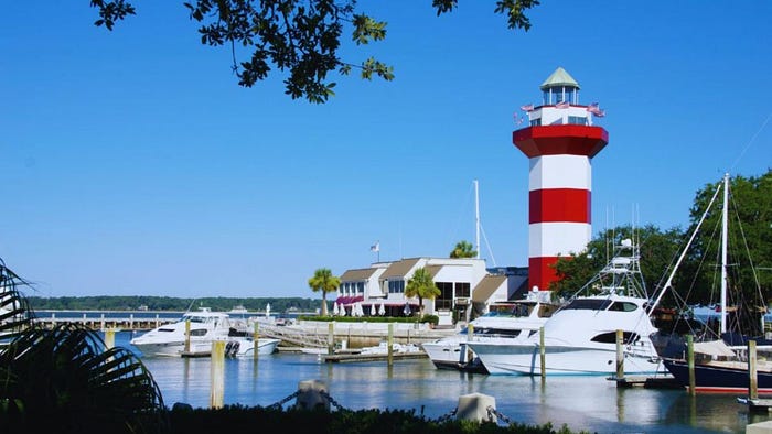 Harbor Town Lighthouse overlooking a calm marina with docked yachts on Hilton Head Island under a clear blue sky.