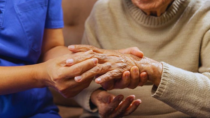A caregiver gently holds an older person's hands, showing compassion and support for someone living with rheumatoid arthritis.