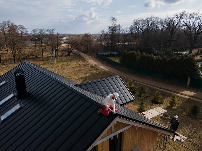 Roofer in helmet ensuring steel roof maintenance to prevent weather damage.