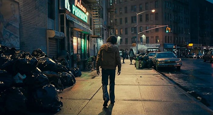 Joaquin Phoenix sebagai Arthur Fleck berjalan di sisi kota Gotham yang kumuh dalam film Joker