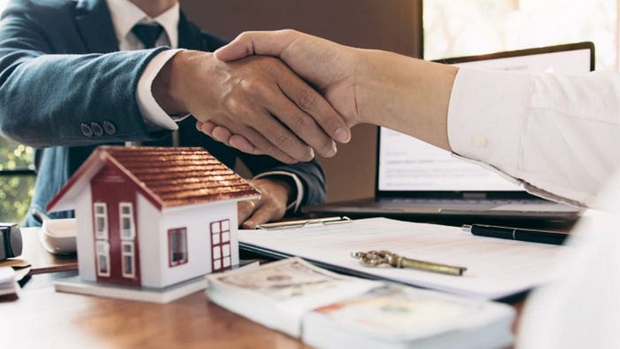 A real estate agent and client shake hands over documents and keys, symbolizing a home purchase in Hilton Head, SC.