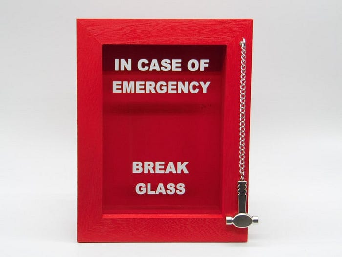 A red case with a glass surface that says “In case of emergency break glass”. There is a little metal hammer hanging on the side by a chain.