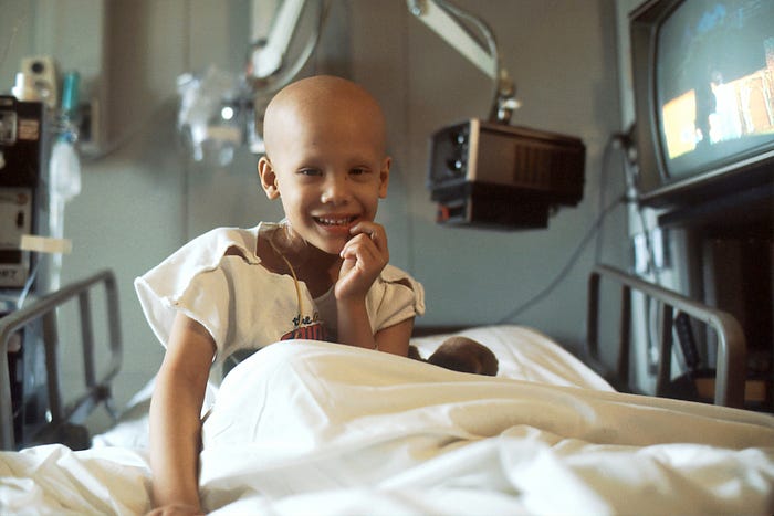 A child on a hospital bed with a shaven head, smiling