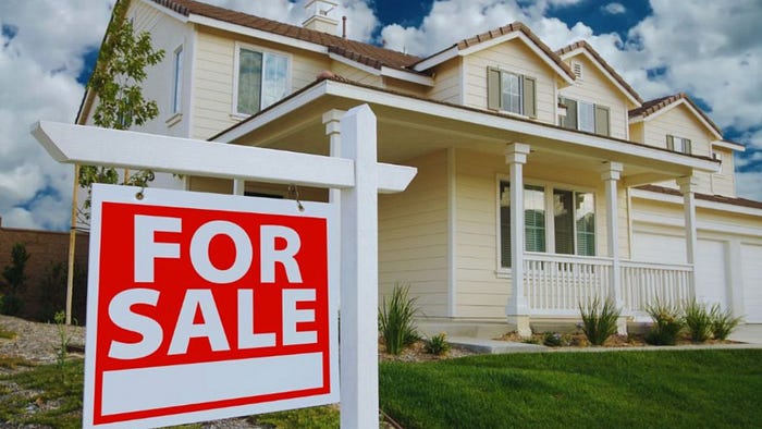 A for sale sign stands in front of a house, indicating the property is available.