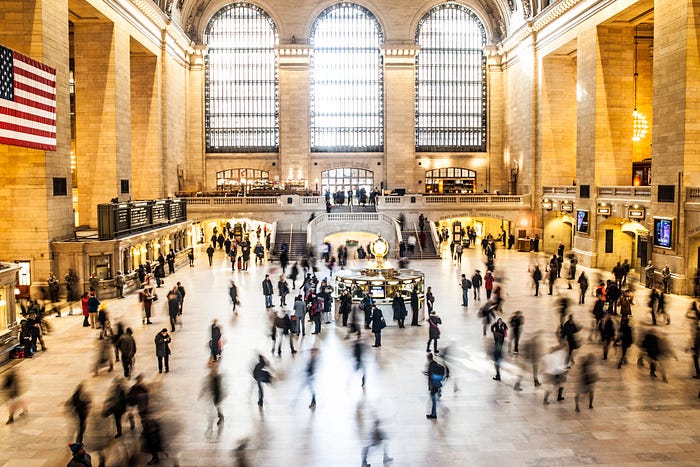A crowd of people moves through a large, open train station