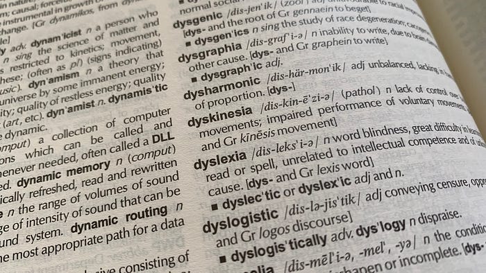 Photograph of a dictionary page from a slanted angle showing the partial definition for dyslexia. The visible part of the definition includes the words: “word blindness” and “unrelated to intellectual competency.”