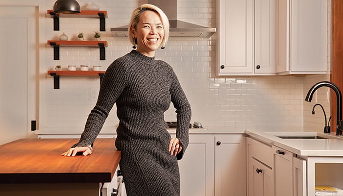 An Asian woman with short, blonde hair — Kat Holmes — stands proudly in a white kitchen.