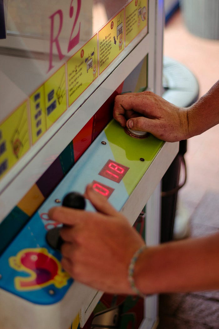 A close up of hands using the handle and button of a claw machine.