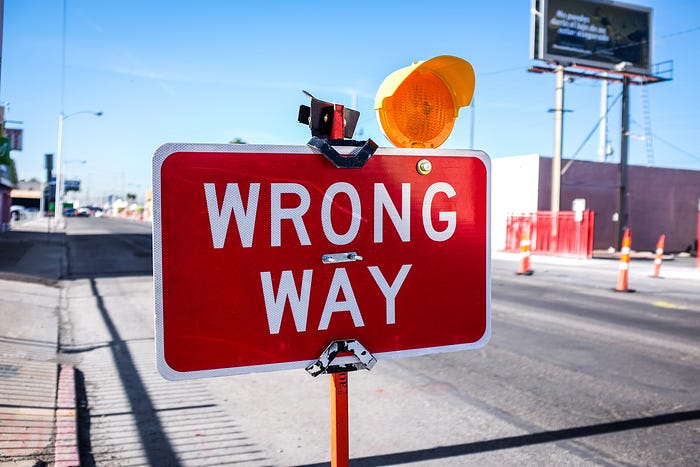 White letters on a red background spell WRONG WAY along a road under construction. A yellow light is mounted on the sign.