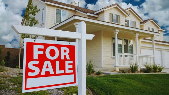 A "For Sale" sign stands in front of a house, indicating it is available for purchase.