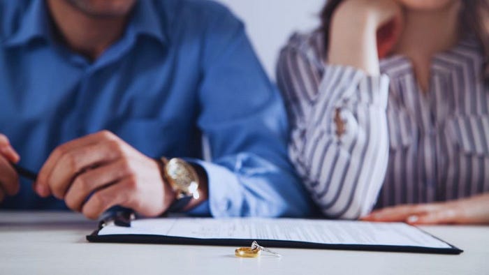 Unhappy couple sitting at a table with a divorce agreement and two wedding rings placed on the table, symbolizing the end of a marriage and the legal process of separation.
