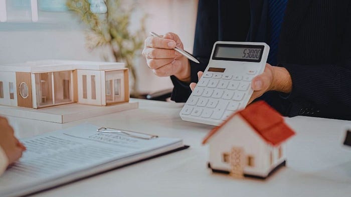 A real estate agent using a calculator at a desk with a model house and paperwork, representing housing costs and real estate budgeting on Hilton Head Island.