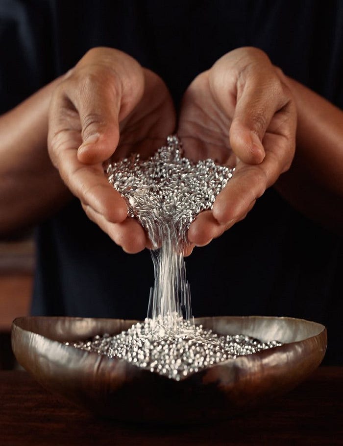 Raw silver granules flowing through hands representing physical silver demand why silver prices are rising in 2026, insights by The Jewelry Gossip.