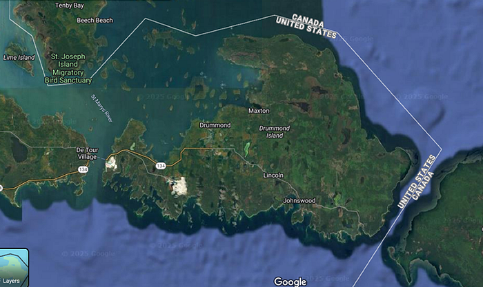 An air-photo map of Drummond Island, Michigan in Lake Huron. On the far western side of the island is a dashed line indicating a ferry route.