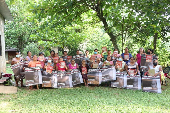 group of women standing and sitting in a yard, with trees surrounding them, holding banners